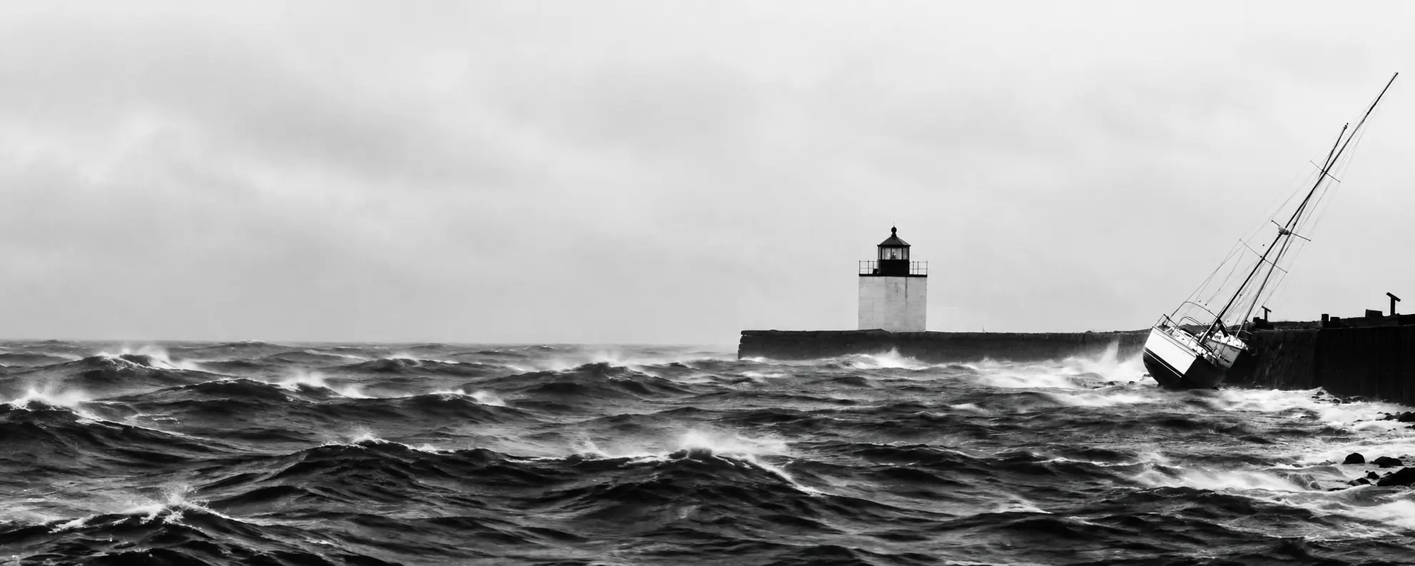 Black-and-white photograph of a sailboat in rough seas against a harbor wall, with a lighthouse in the distance, by Thomas Stirling
